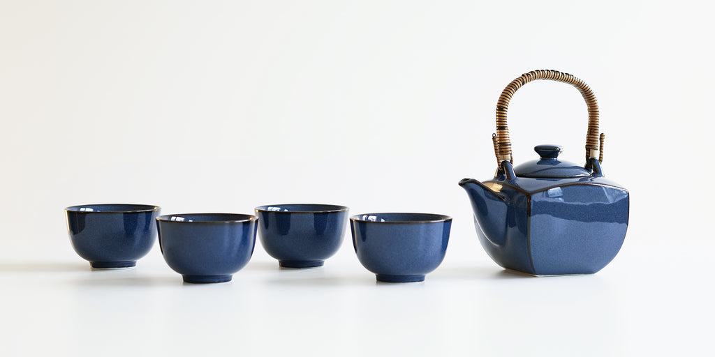 Side view of a dark blue ceramic tea set, with four cups on the left and a pot on the right.