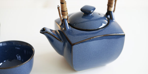 Close up of a dark blue ceramic teapot, with squared sides and black along the edges.