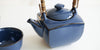 Close up of a dark blue ceramic teapot, with squared sides and black along the edges.