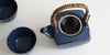 Top view of a dark blue ceramic teapot, showing the hand-wrapped bamboo handle and stainless steel infuser.