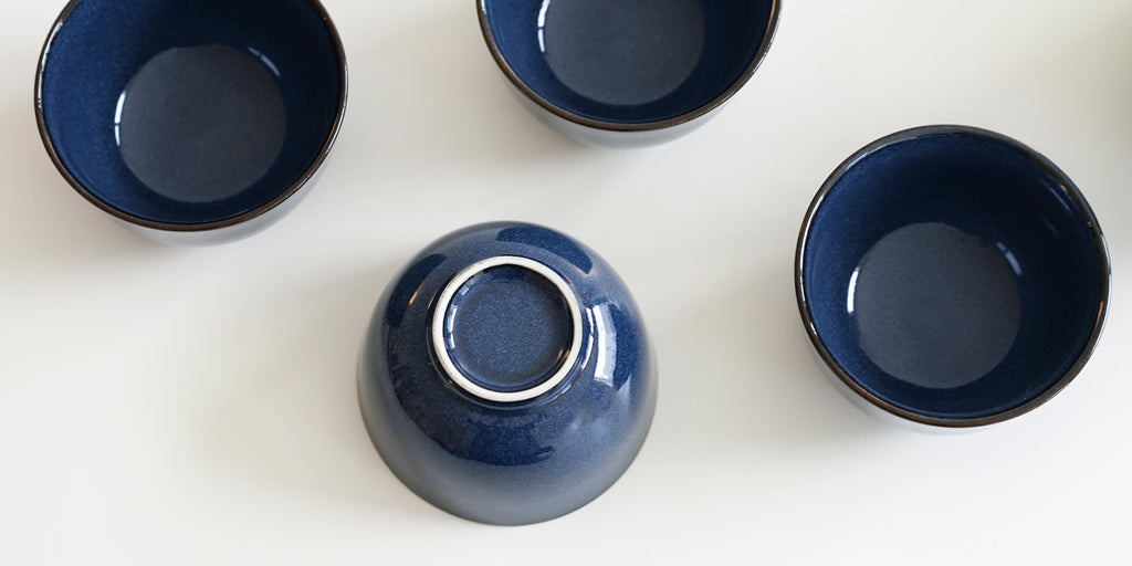 Close up of the bottom of a dark blue ceramic cup. The rim of the foot is unglazed and white.