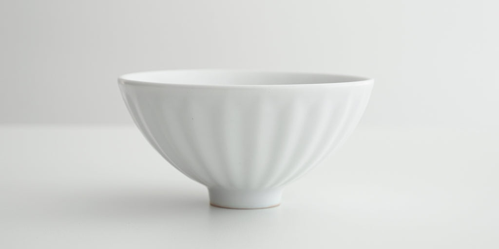 Side view of a white stoneware bowl with soft ridges radiating from the base on the outside.