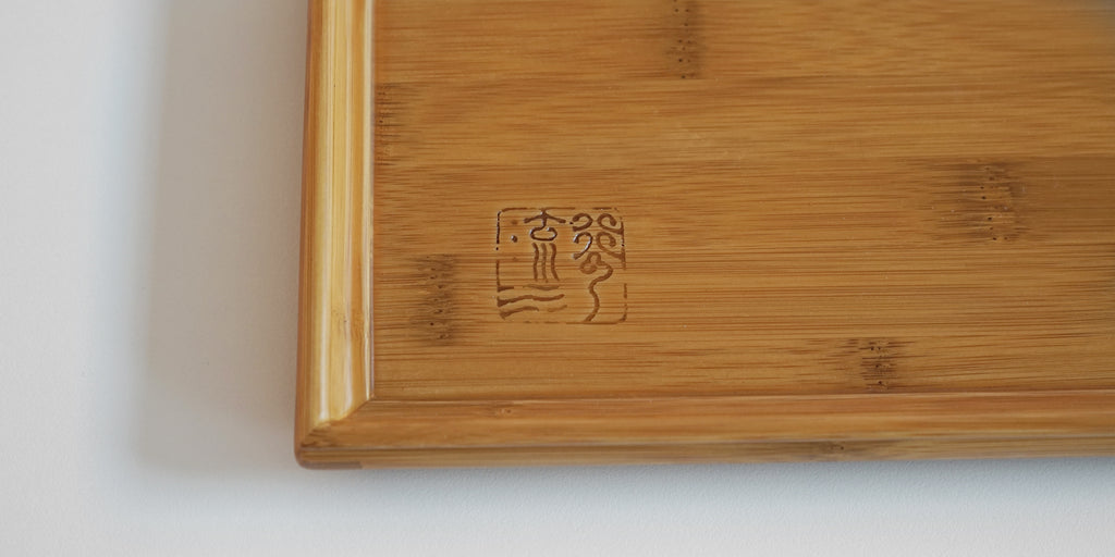 Close up of the maker's mark carved into the corner of a bamboo tea tray.