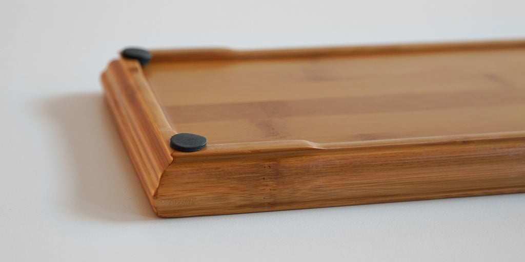 Close up of the underside of a bamboo tray. The foot elevates the tray slightly, and there are rubber feet on each corner.