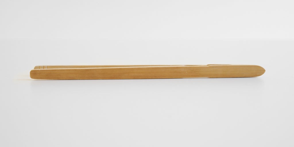 Side view of a pair of bamboo tongs, showing the grain running along the outside.