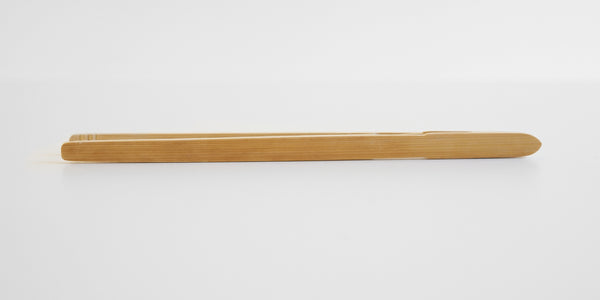 Side view of a pair of bamboo tongs, showing the grain running along the outside.