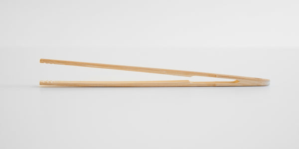 Side view of a pair of bamboo tea tongs on a white background. The tongs are joined at the top, with a small cutout to improve flexibility.
