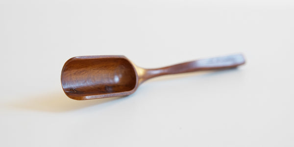 Cherrywood scoop lying askew on a white table. The scoop is highlighted, with the handle extending off into the background out of focus.