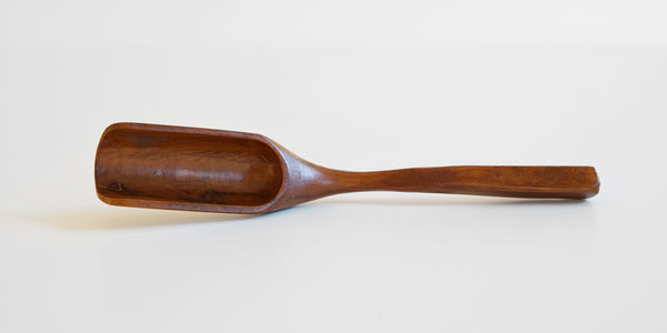Cherrywood tea scoop resting askew on a white table, showing the inside of the scoop.