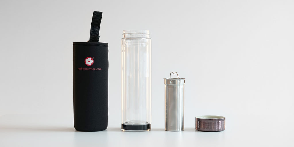 From left to right: a black cozy with a red logo to put the thermos in, the double-walled glass thermos, the stainless steel strainer basket, and the screw-on lid.