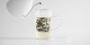 Side view of a glass up with a tea infuser. Water is being added, causing the leaves to churn. A glass lid is placed off to the side.