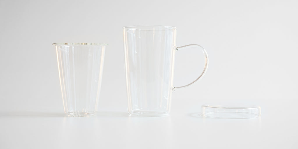Side view of each part of the glass infuser cup. From left to right, the infuser, the cup, and the lid.