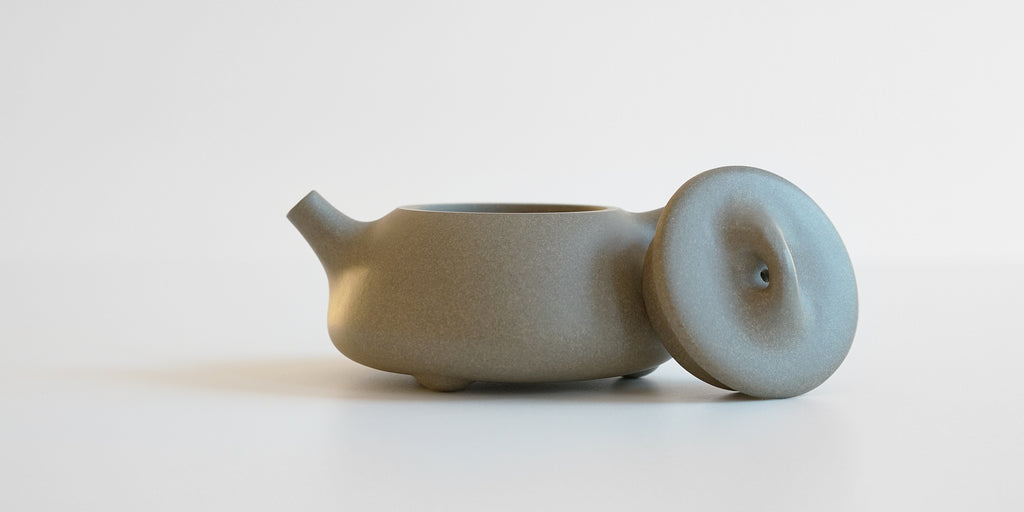 Side view of a gray duanni yixing teapot. The lid is facing the camera, resting against the handle.