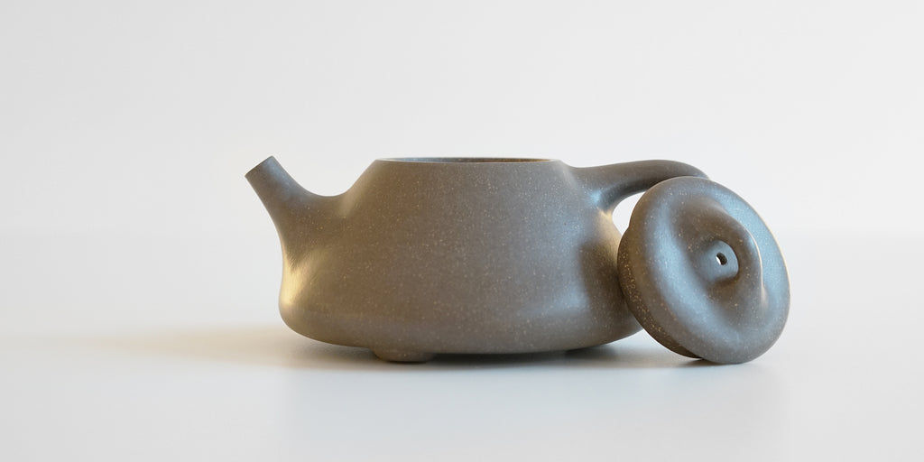 Side view of a gray duanni yixing teapot, with the lid facing the camera resting against the handle.