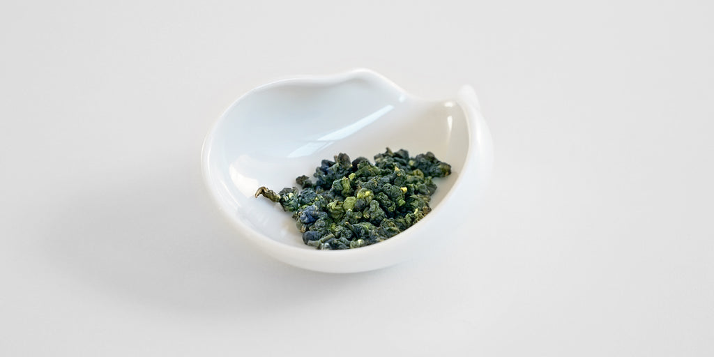 White ceramic tea dish from the wider back side, with Formosa oolong tea leaves inside.