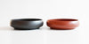 Two tea trays side by side, a black one on the left and a terracotta-colored one on the right.