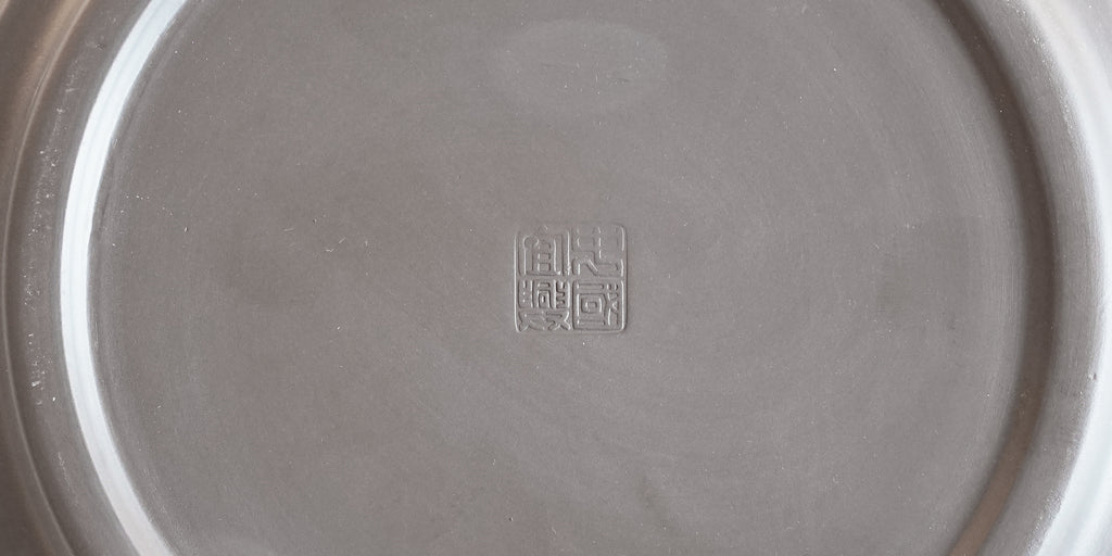 Close-up view of the bottom of a black tea tray, with a makers mark stamped in the middle.