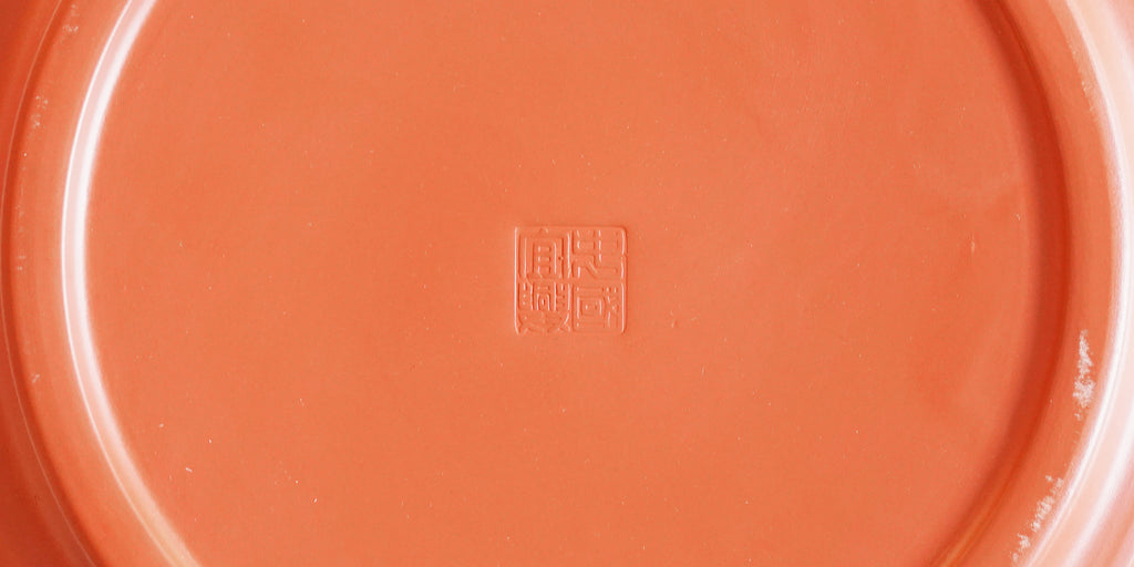 Close-up view of the bottom of a terracotta-colored tea tray, with a makers mark stamped in the middle.