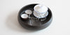  A white gaiwan, a glass server, and two teacups in a round black tea tray.