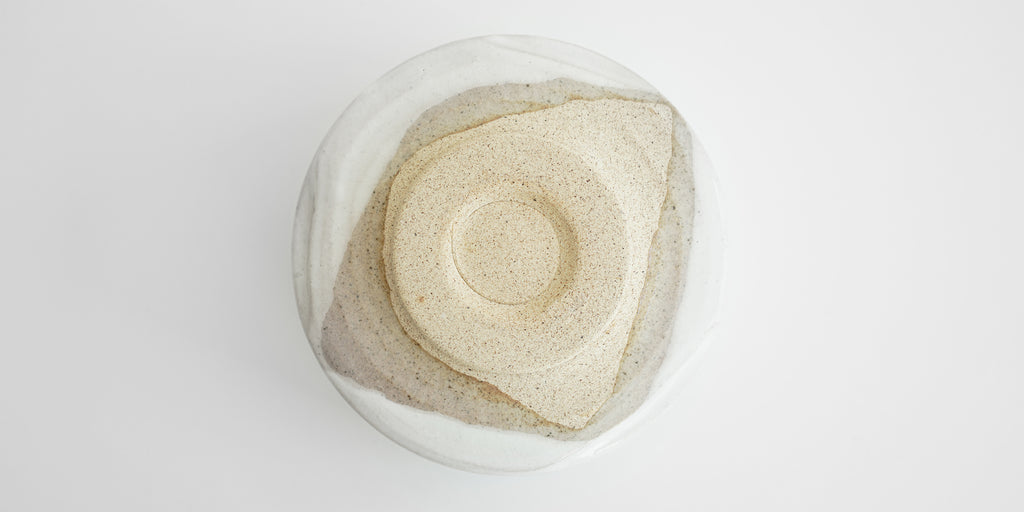 The bottom of a white bowl. The foot is a beige color, and unglazed.