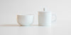 Side view of a competition brewing set. A small white bowl is on the left, and the brewing vessel, similar to a teapot but without a spout, is on the right.