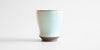 Side view of a small blue-green celadon drinking cup in a shape similar to a tulip glass.