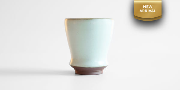 Side view of a small blue-green celadon drinking cup in a shape similar to a tulip glass. A gold ribbon in the top right corner reads "New Arrival"