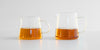 Two glass servers side by side with tea in them, a smaller one on the left, larger on the right.
