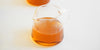 A glass server with tea in it, steam gathering above the tea. A second server is blurred in the background.