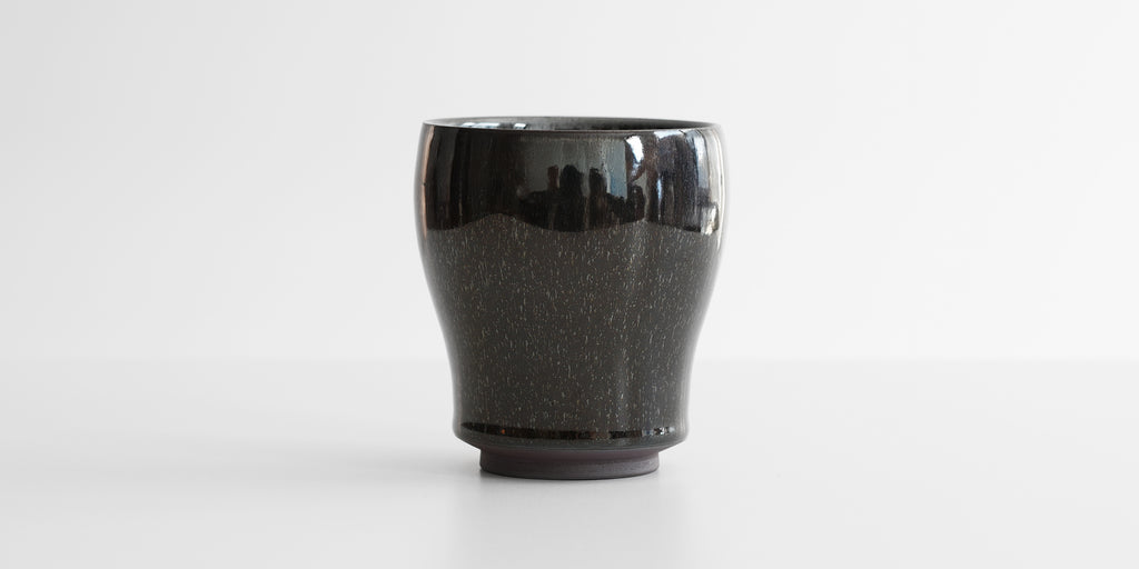 A side-view of a jian-ware cup, displaying the hare's fur texture on the otherwise black glaze.