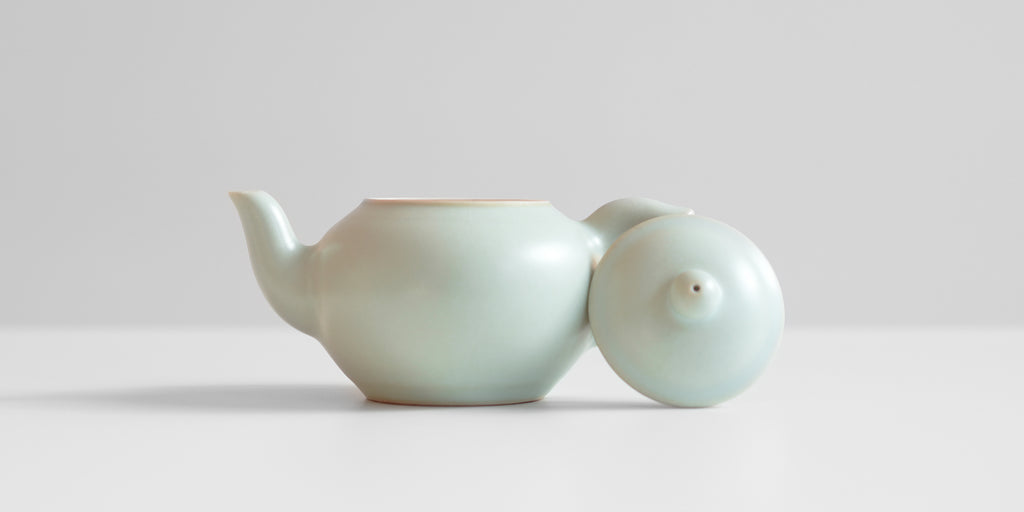 A side view of a celadon teapot. The lid is resting against the handle.