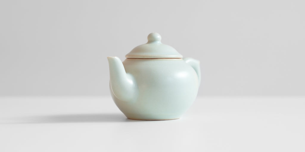 A front-view of a celadon teapot showing the spout.