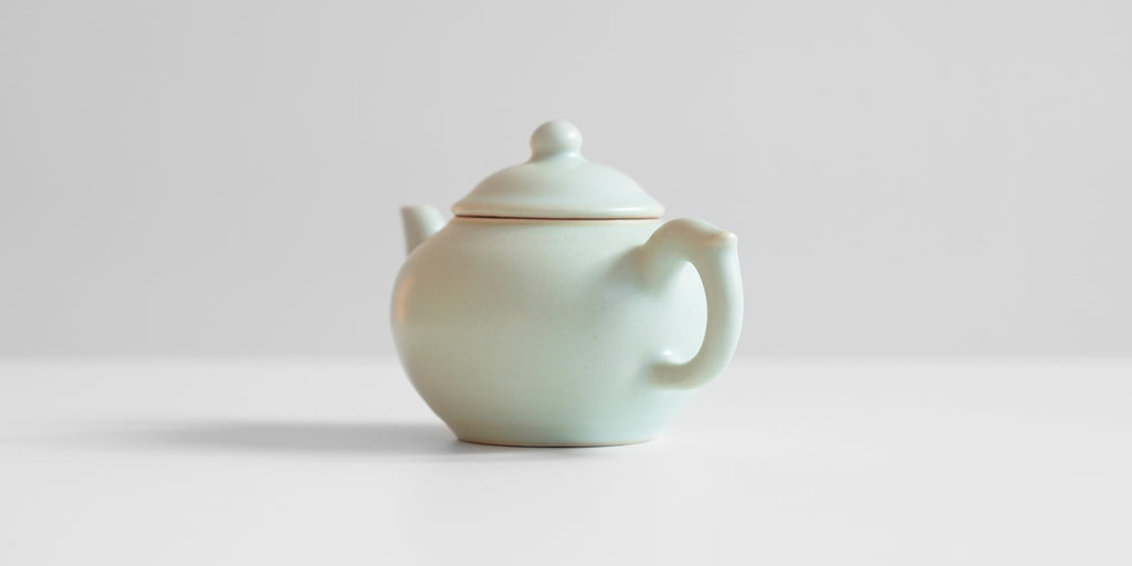 A back view of a celadon teapot showing the handle.