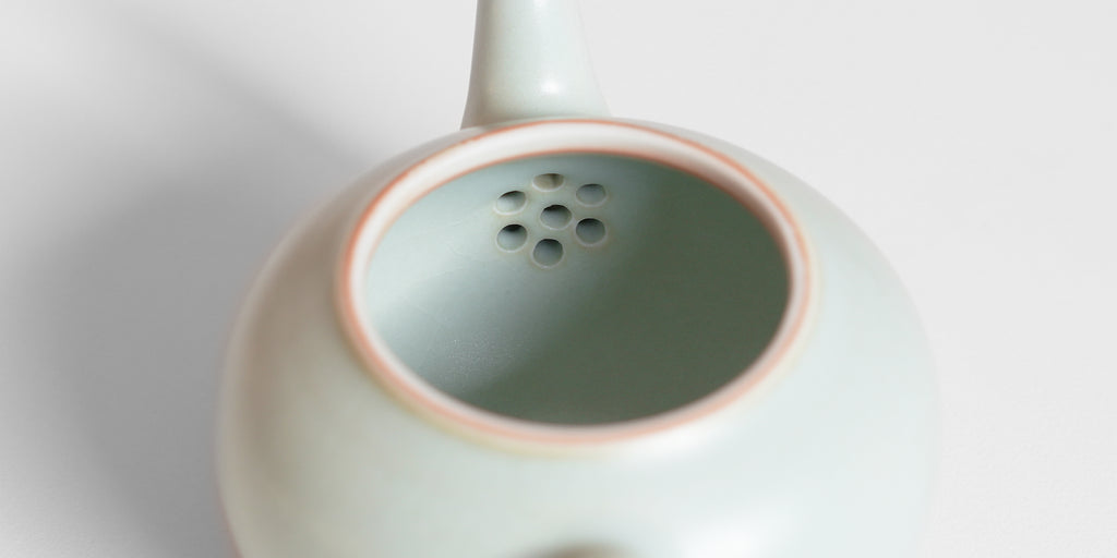 A close-up of a celadon teapot showing the strainer holes on the inside of the ceramic.