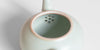 A close-up of a celadon teapot showing the strainer holes on the inside of the ceramic.