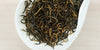 A white dish containing dry black tea leaves.