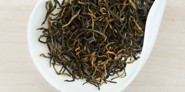 A white dish containing dry black tea leaves.