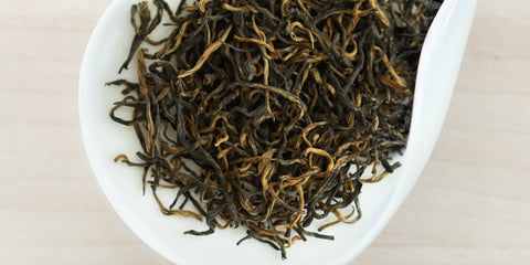 A white dish containing dry black tea leaves.