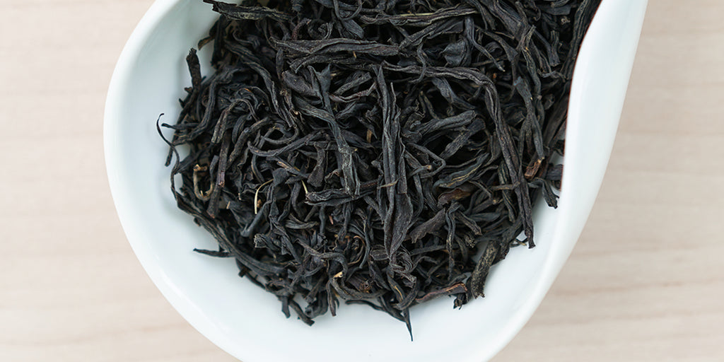 A white dish containing dry black tea leaves.