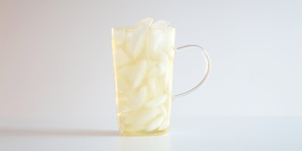A glass cup filled with ice and jasmine tea on a white background.