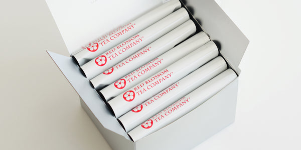 A silver box with 7 white bags of tea showing the Red Blossom Tea Company logo inside.