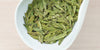 A white dish containing dry green tea leaves.