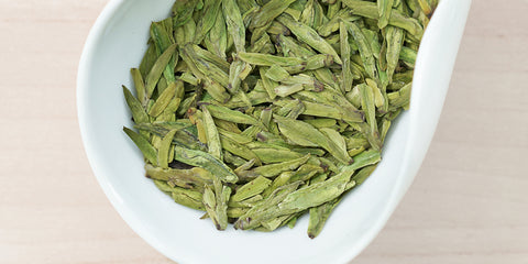 A white dish containing dry green tea leaves.