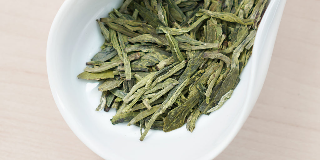 A white dish containing dry green tea leaves.