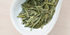 A white dish containing dry green tea leaves.