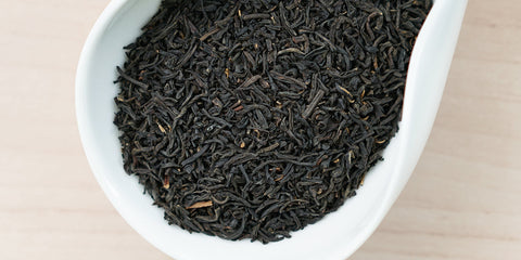 A white dish containing dry black tea leaves.