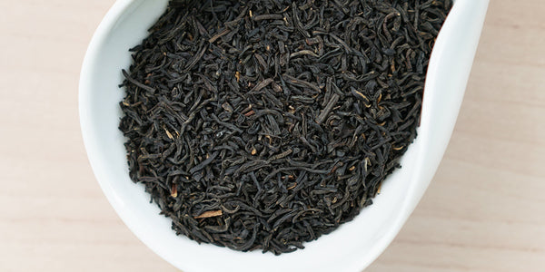 A white dish containing dry black tea leaves.