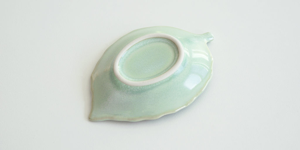 The bottom of a leaf trivet, light green with a glossy finish. The foot is unglazed and white.