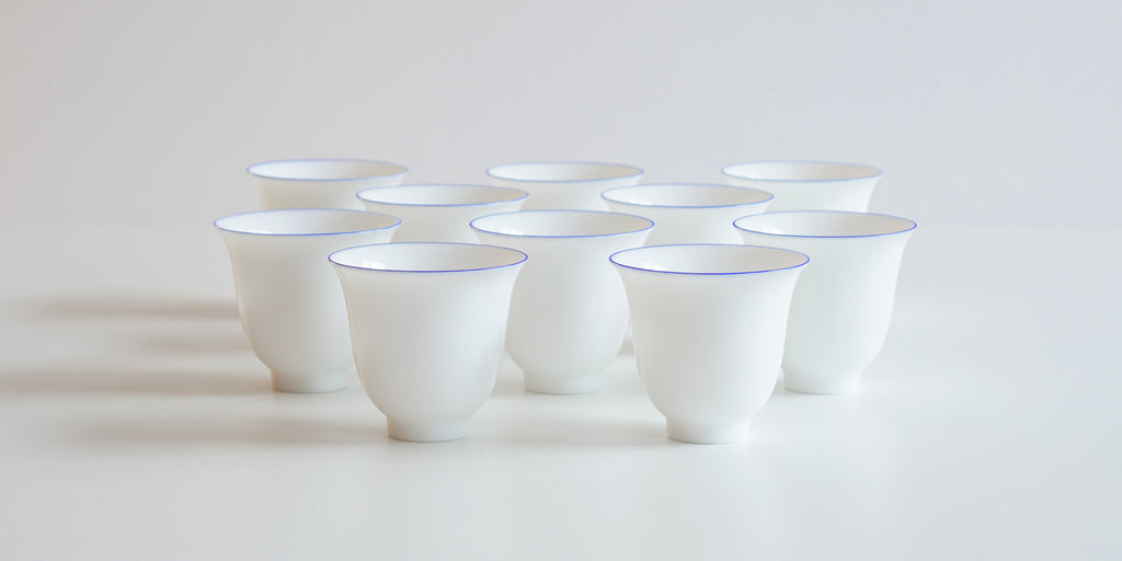 Ten white porcelain cups with a blue ring around the lip arranged in a pattern on a white background.