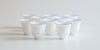 Ten white porcelain cups with a blue ring around the lip arranged in a pattern on a white background.